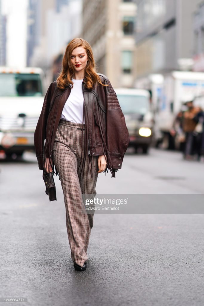 NEW YORK, NEW YORK - FEBRUARY 11: Larsen Thompson wears a brown fringed leather jacket, a white t-shirt, houndstooth pattern printed flared pants, a bag, outside Coach, during New York Fashion Week Fall Winter 2020, on February 11, 2020 in New York City. (Photo by Edward Berthelot/Getty Images)
